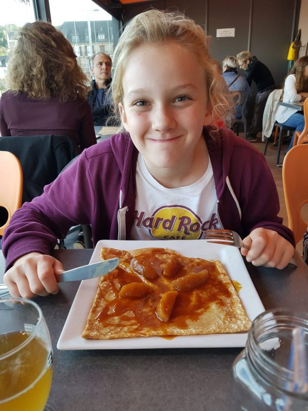 enfant qui déguste une spécialité de crêpes de la région au caramel et pommes